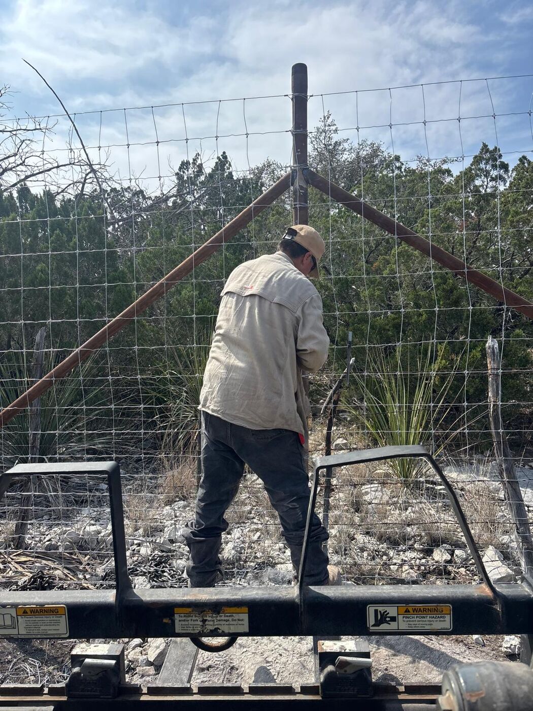 Crew member tying game fence wire at a welded pipe corner brace
