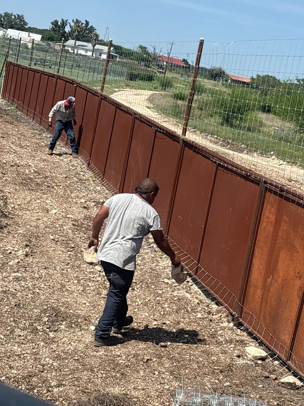 Crew working along a tall steel privacy and game fence line