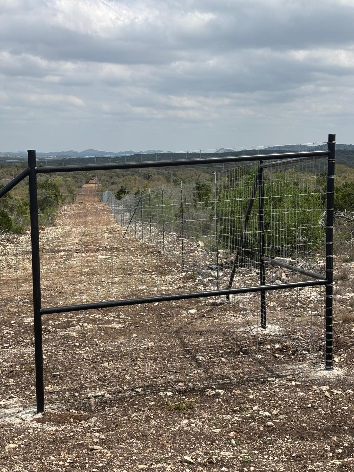Welded steel corner post and a game-proof fence line running to the horizon in the Texas Hill Country