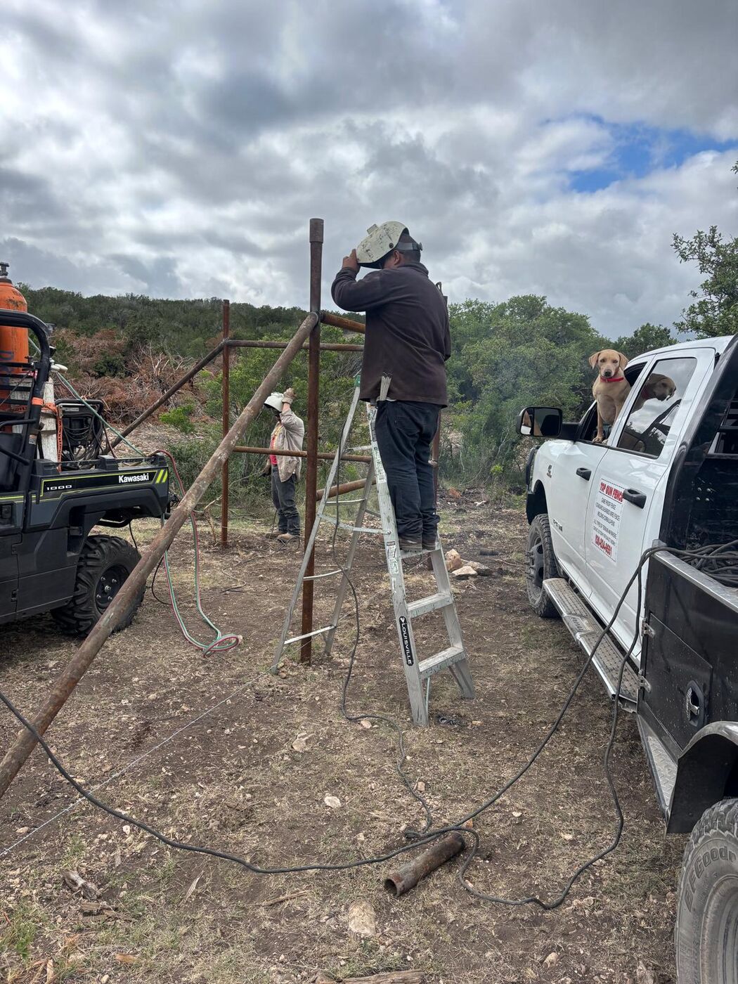 Welder on a ladder building a pipe corner brace next to the Top Gun Fence truck